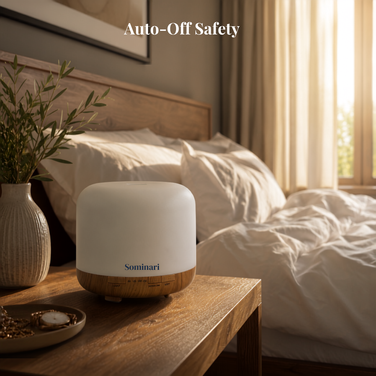 A Sominari essential oil diffuser sits on a wooden bedside table in a softly lit bedroom. The diffuser has a matte white top and a natural wood base.